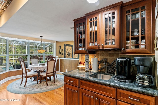 kitchen with pendant lighting, backsplash, dark stone counters, sink, and light wood-type flooring