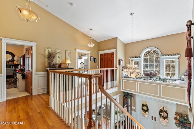 hallway featuring a notable chandelier, light wood-type flooring, and lofted ceiling