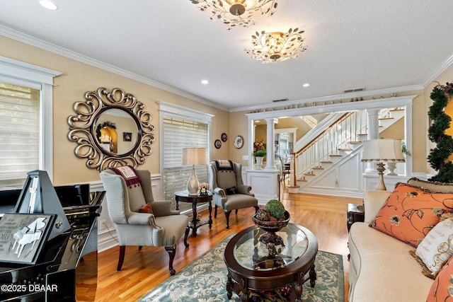 living room featuring light hardwood / wood-style floors, ornate columns, crown molding, and an inviting chandelier