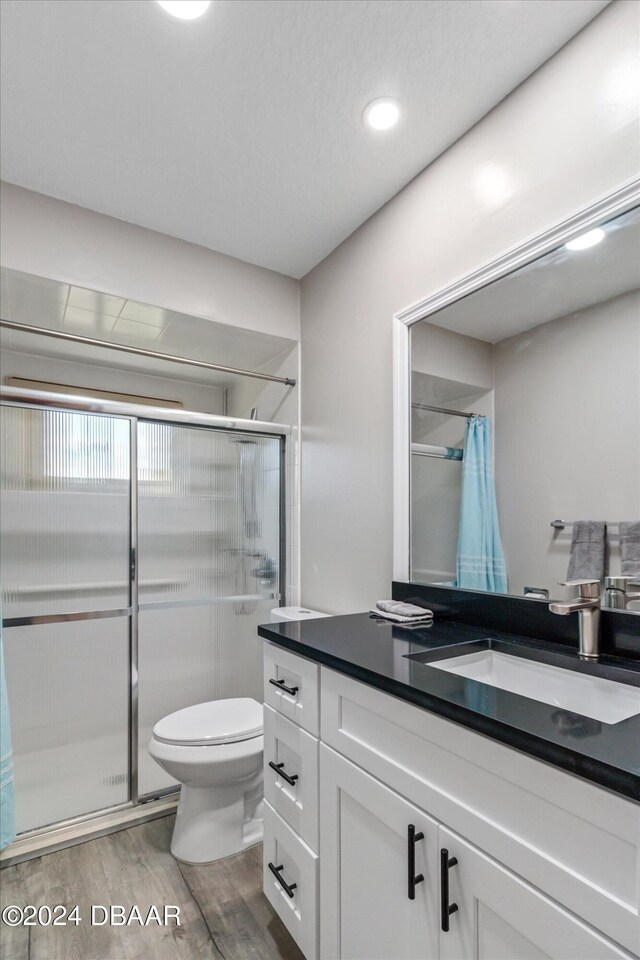 bathroom featuring hardwood / wood-style floors, vanity, toilet, and a shower with door