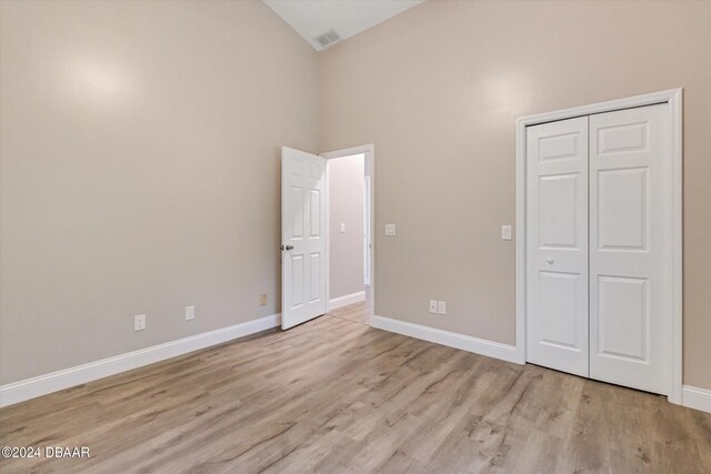 unfurnished bedroom featuring a closet, light wood-type flooring, and high vaulted ceiling