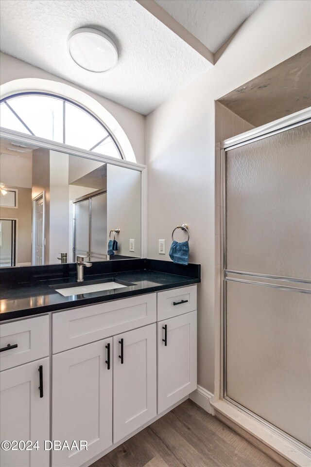 bathroom with wood-type flooring, vanity, a shower with door, and a textured ceiling