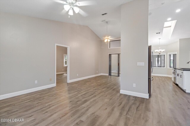 unfurnished living room with light hardwood / wood-style flooring, a skylight, sink, and ceiling fan with notable chandelier