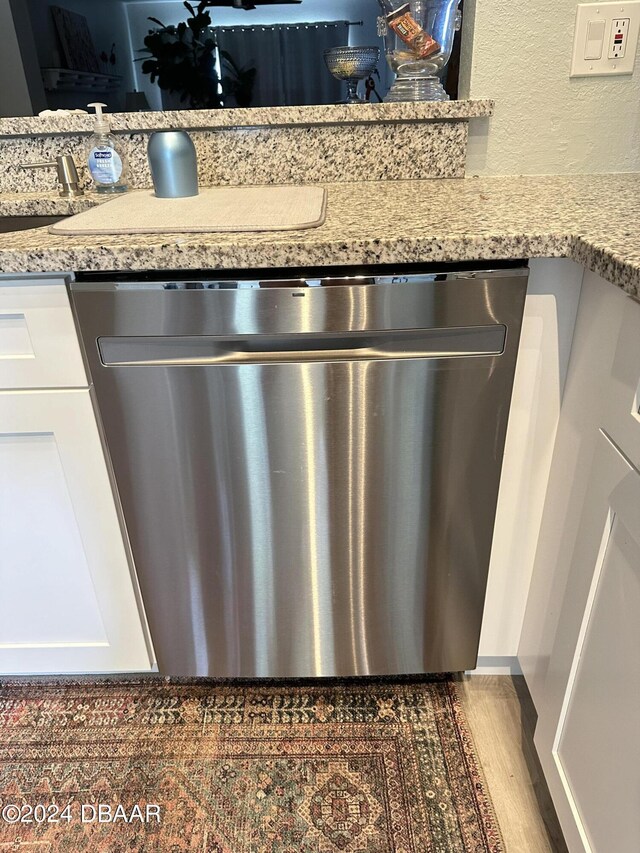 1021 Alabama Ave, Holly Hill, FL 32117 - kitchen view of stainless steel dishwasher, white cabinets, light stone countertops, and wood finished floors