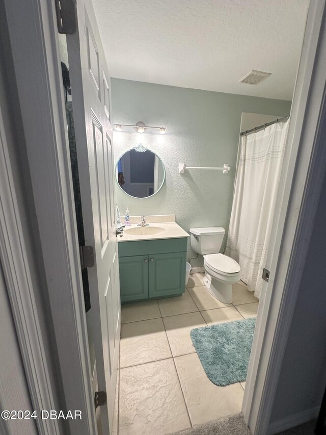 1021 Alabama Ave, Holly Hill, FL 32117 - bathroom featuring a textured wall, toilet, vanity, tile patterned flooring, and a textured ceiling