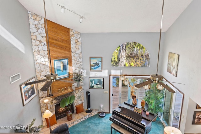 living room featuring ceiling fan, a stone fireplace, a towering ceiling, and wooden walls