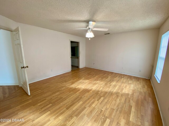 unfurnished room with ceiling fan, a textured ceiling, and light wood-type flooring