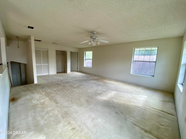 carpeted empty room featuring a wealth of natural light, a textured ceiling, and ceiling fan