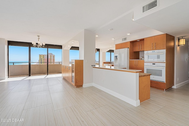 kitchen featuring a wall of windows, kitchen peninsula, white appliances, and a chandelier