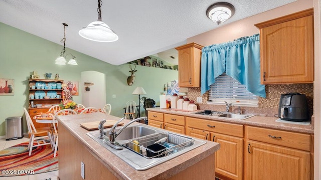 kitchen featuring decorative light fixtures, tile patterned floors, a center island with sink, and sink