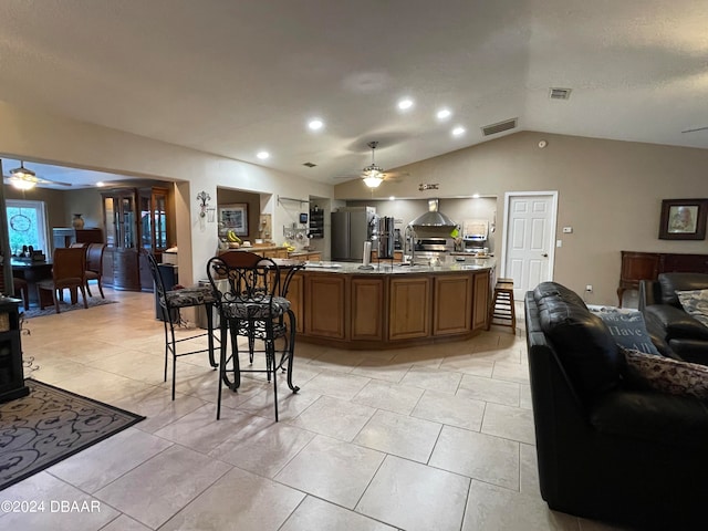 kitchen with stainless steel fridge, light tile patterned floors, lofted ceiling, and wall chimney range hood