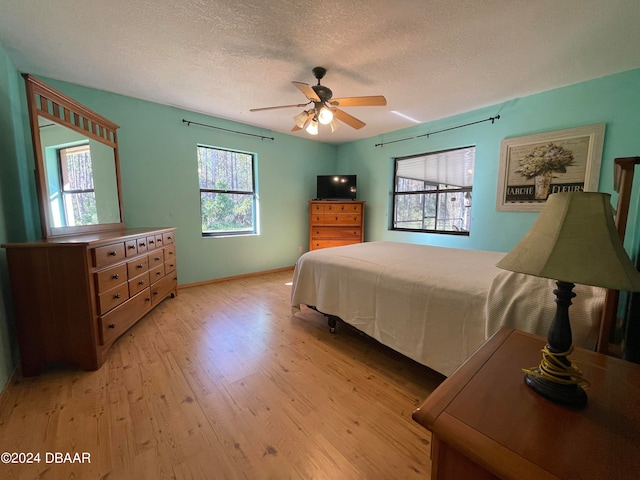 bedroom with light hardwood / wood-style floors, ceiling fan, multiple windows, and a textured ceiling