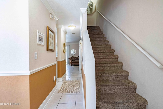 stairs featuring ornate columns, a textured ceiling, tile patterned floors, and ornamental molding