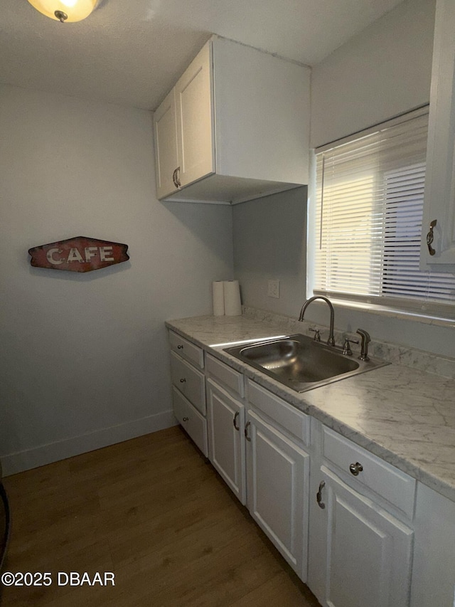 kitchen with light countertops, light wood-style floors, white cabinets, a sink, and baseboards