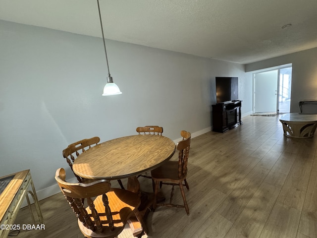 dining space with a textured ceiling, baseboards, and wood finished floors