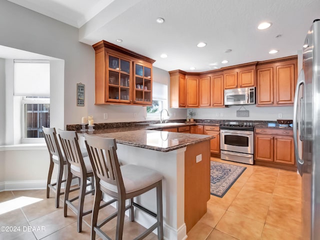 kitchen with sink, kitchen peninsula, dark stone countertops, a kitchen bar, and appliances with stainless steel finishes