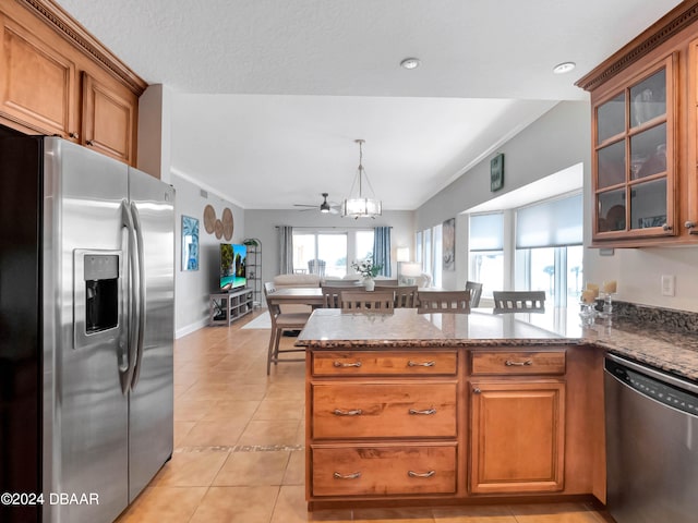 kitchen featuring kitchen peninsula, appliances with stainless steel finishes, dark stone counters, light tile patterned floors, and hanging light fixtures