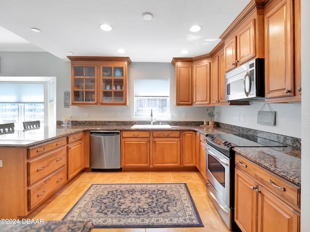 kitchen with sink, dark stone countertops, light tile patterned floors, kitchen peninsula, and stainless steel appliances