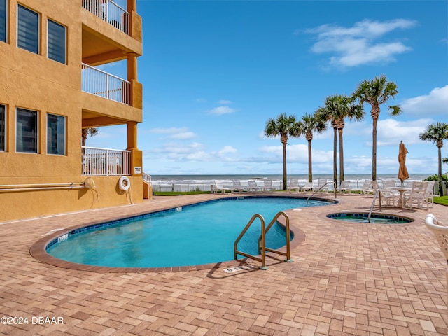 view of pool featuring a water view, a hot tub, and a patio area