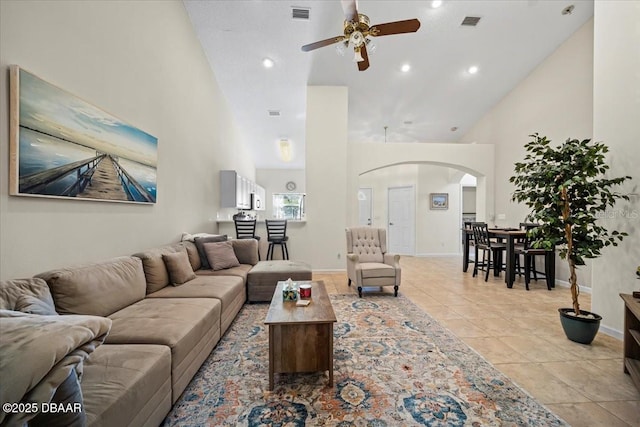 living area featuring arched walkways, high vaulted ceiling, light tile patterned floors, visible vents, and baseboards