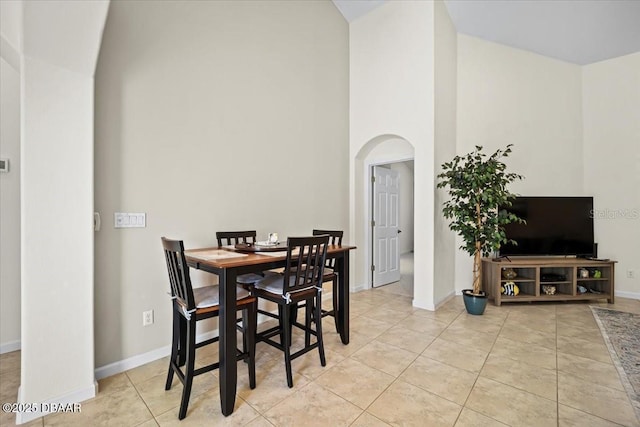 dining room with arched walkways, light tile patterned flooring, a towering ceiling, and baseboards