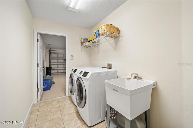 laundry area with a textured ceiling, light tile patterned flooring, laundry area, a sink, and washing machine and clothes dryer