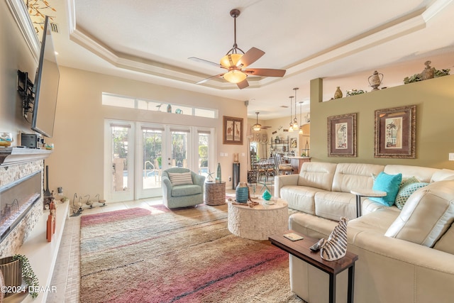 living room featuring french doors, a raised ceiling, ceiling fan, and a stone fireplace