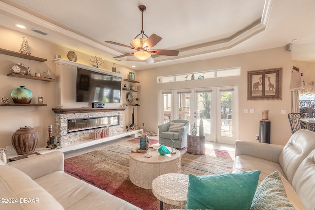 tiled living room with ceiling fan, a raised ceiling, ornamental molding, and french doors