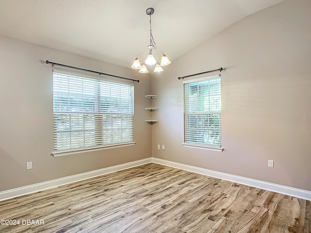 unfurnished room with lofted ceiling, an inviting chandelier, and hardwood / wood-style flooring