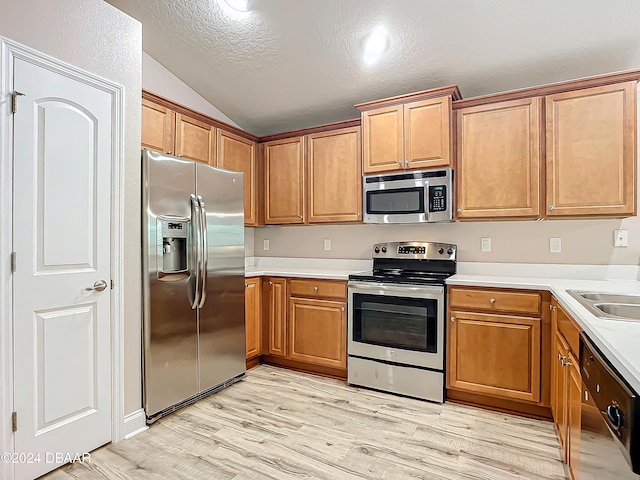 kitchen featuring appliances with stainless steel finishes, light wood-type flooring, a textured ceiling, sink, and lofted ceiling