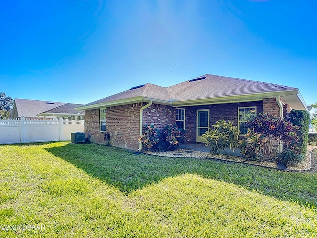 rear view of property with cooling unit and a lawn