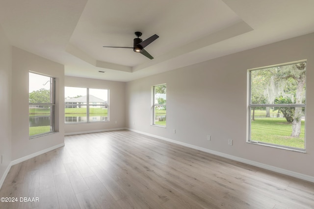 spare room featuring light hardwood / wood-style flooring, a raised ceiling, ceiling fan, and plenty of natural light