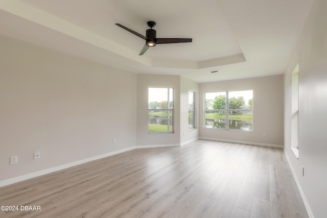 spare room with ceiling fan, a water view, a raised ceiling, and light wood-type flooring