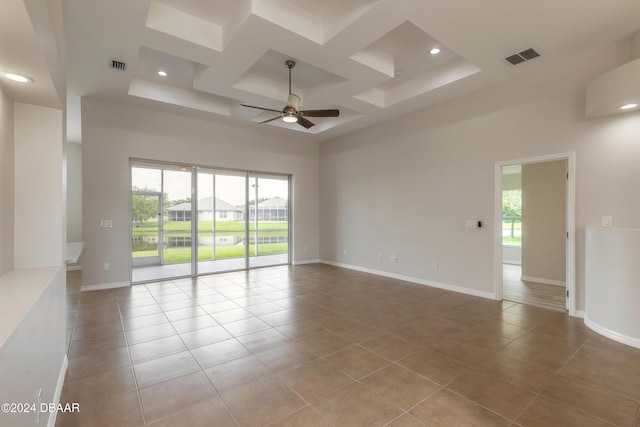 empty room with ceiling fan, a high ceiling, coffered ceiling, and light tile patterned floors