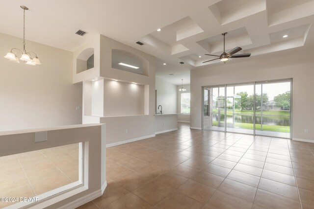 tiled empty room with a high ceiling, coffered ceiling, and ceiling fan with notable chandelier