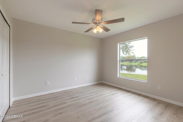 unfurnished bedroom with a closet, light wood-type flooring, a water view, and ceiling fan