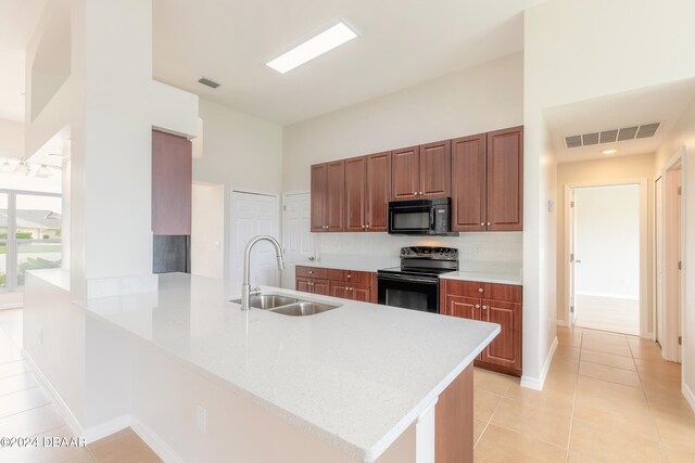 kitchen featuring sink, black appliances, kitchen peninsula, light tile patterned floors, and a towering ceiling