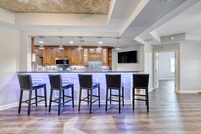 kitchen featuring stainless steel appliances, kitchen peninsula, dark hardwood / wood-style flooring, a breakfast bar area, and a tray ceiling