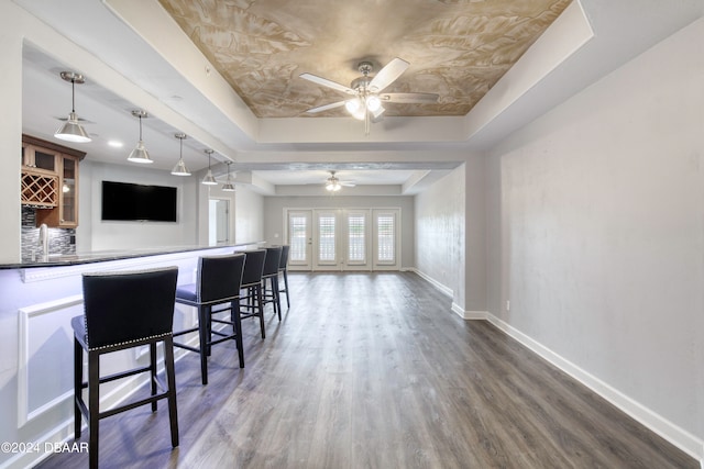 kitchen with a kitchen bar, ceiling fan, decorative light fixtures, a raised ceiling, and dark wood-type flooring