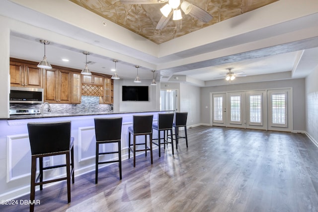 kitchen featuring wood-type flooring, kitchen peninsula, ceiling fan, a breakfast bar, and a tray ceiling