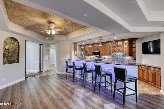 kitchen featuring stainless steel appliances, kitchen peninsula, a breakfast bar area, a tray ceiling, and light wood-type flooring