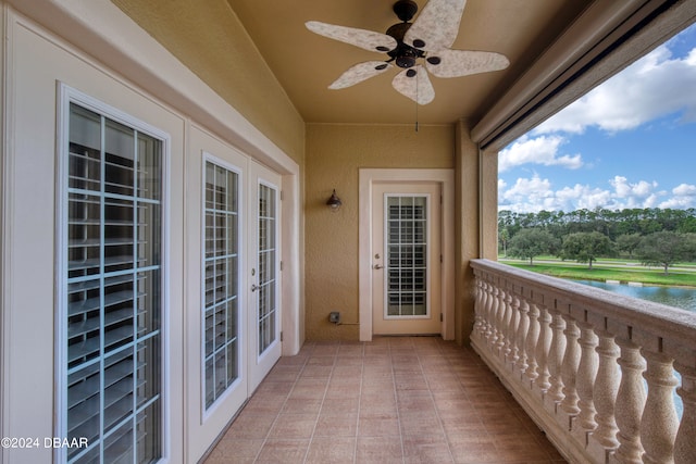 balcony with ceiling fan, a water view, and french doors