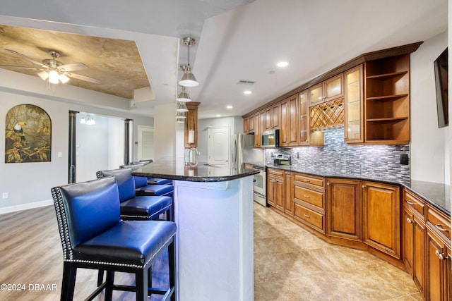 kitchen with stainless steel appliances, light hardwood / wood-style floors, a breakfast bar, backsplash, and hanging light fixtures