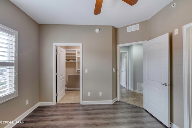 unfurnished bedroom with dark wood-type flooring, multiple windows, a spacious closet, and ceiling fan