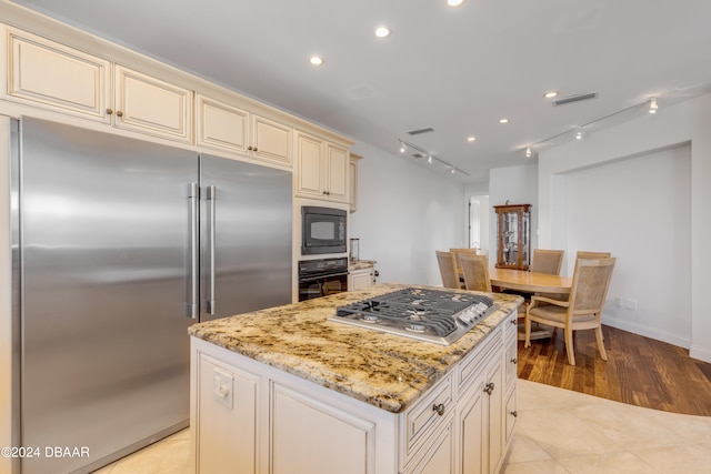 kitchen with black appliances, cream cabinets, light stone countertops, light hardwood / wood-style flooring, and a center island