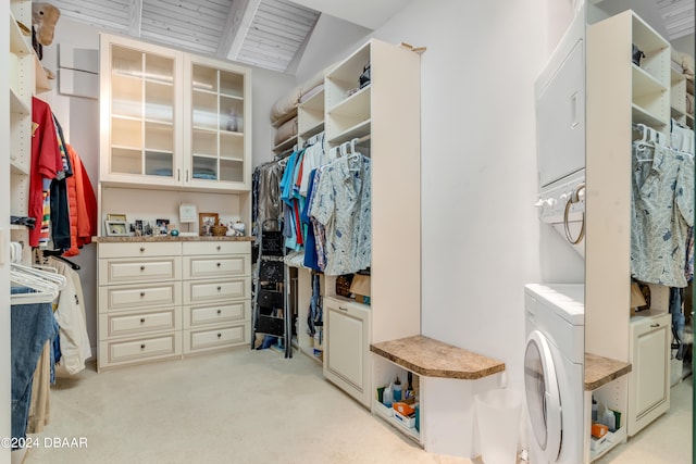 walk in closet with stacked washer and dryer, light carpet, and vaulted ceiling with beams