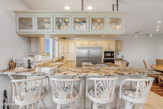 kitchen featuring black appliances, kitchen peninsula, light stone counters, and a breakfast bar area