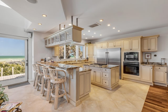 kitchen featuring black appliances, light stone counters, cream cabinets, a breakfast bar area, and a kitchen island