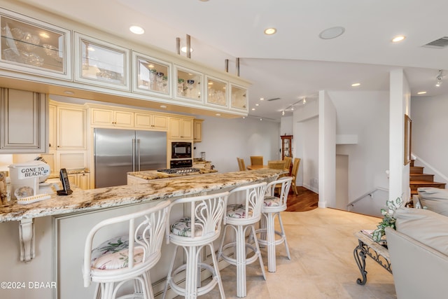 kitchen featuring built in appliances, kitchen peninsula, light stone countertops, a breakfast bar area, and cream cabinetry