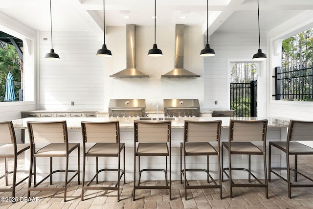 kitchen featuring brick floor, hanging light fixtures, wall chimney range hood, and decorative backsplash